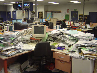 A very messy office, with desks buried under piles of papers and folders