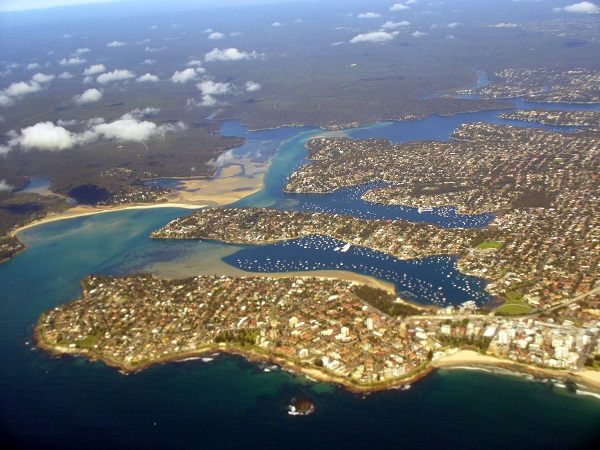 Aerial photo of an estuary on the Sydney coast, with a river mouth, sand flats, moored boats and suburbs along the shore