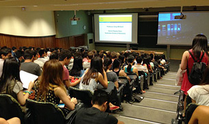 Students seated in a university lecture theatre facing two projection screens