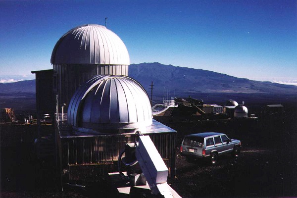 The domed buildings of the Mauna Loa Observatory in Hawaii, with a volcano in the background